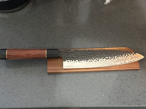 Customer's Gyuto Japanese Chef Knife with a hammered blade and rosewood handle resting on its wooden sheath.