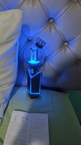 Reviewer's BTS Official Light Stick Ver.4 glowing blue, with its top part open, next to a manual.
