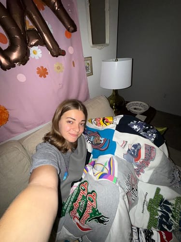 Customer smiling on a couch, wrapped in their colorful Project Repat T-Shirt Quilt.