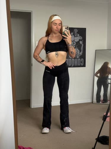 Customer taking a full-length mirror selfie in the black Reverie Flares, showing the cross-front waist.