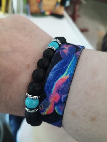 Close-up of a reviewer's wrist wearing the colorful Stay The Course Bracelet with a sea turtle design, next to a beaded bracelet.