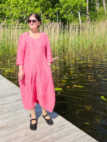 Reviewer wearing the raspberry Balloon Crinkled Dress while standing on a wooden dock.