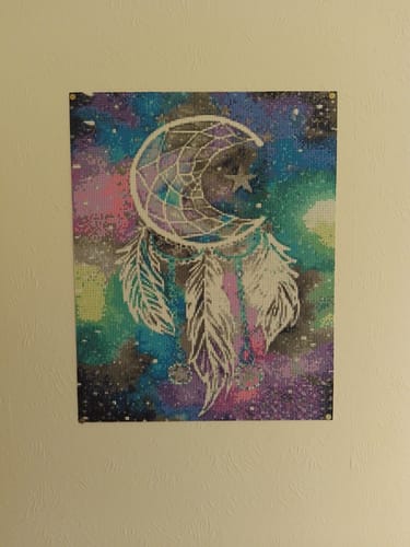 Klant toont de voltooide Dromenvanger diamond painting met een kleurrijke achtergrond die aan een muur hangt.
