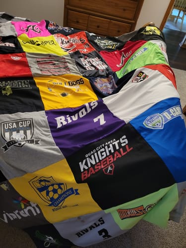 Customer's colorful Double Sided T-Shirt Quilt spread across a bed, featuring various sports logos and designs.
