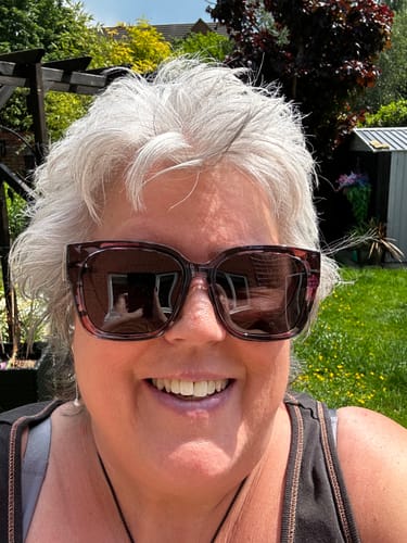 Reviewer smiling outdoors while wearing the large, floral frame Polarized Fit Over Sunglasses.