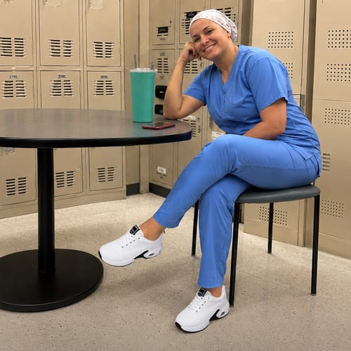Reviewer in blue scrubs relaxing in a locker room while wearing white Ortho Walk 2.0™ shoes.