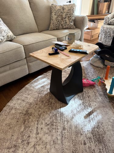 Reviewer's black Tulipe end table leg with a temporary plywood top, placed next to a sofa in a living room.