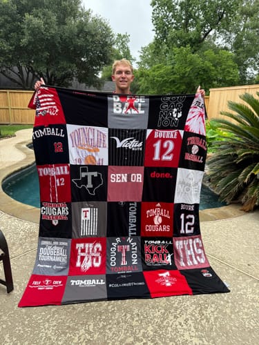 Customer holding a large Project Repat T-Shirt Quilt made from red, black, and white t-shirts outdoors.