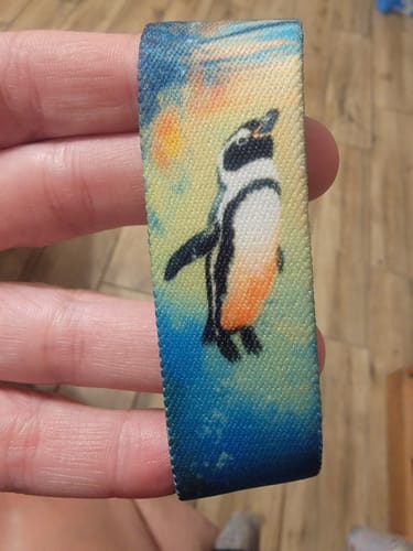 Customer holding a colorful fabric bracelet from the Penguin Pack, which features an artistic penguin design.
