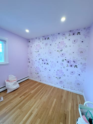 Customer's room showing the beautiful Leah Wallpaper with purple flowers on an accent wall.