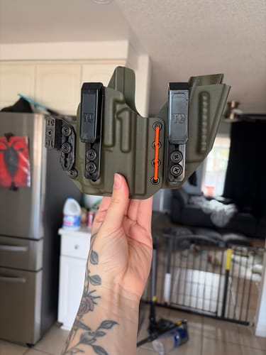 A reviewer holds their olive green AXIS ELITE holster, showing the black clips and orange shock cord.