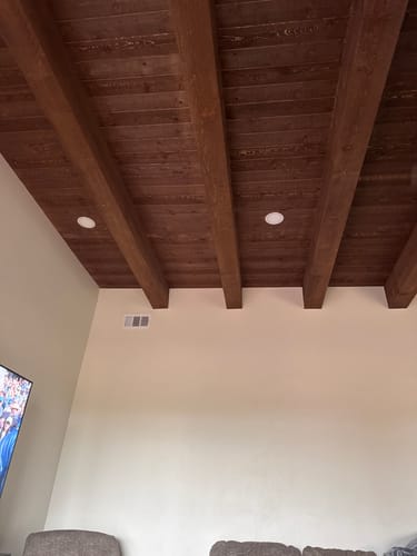 A customer's living room wall painted in Cottage White, shown below a dark wood-beamed ceiling.