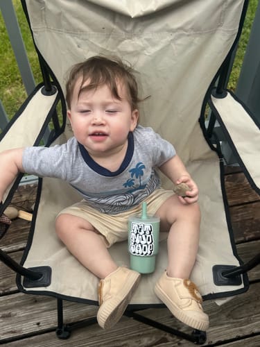 Customer's custom vinyl sticker on a child's green cup, held by a toddler in a chair.