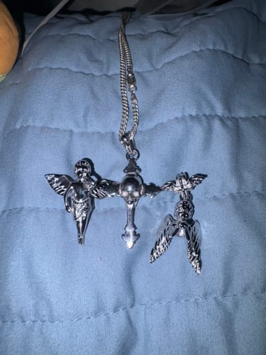 Reviewer's Angel of Death Pendant with two angel figures and a central skull cross, lying on a blue comforter.