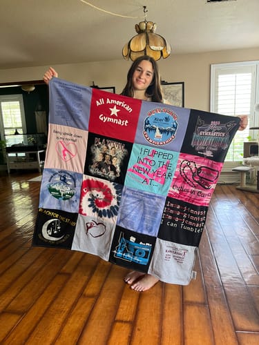 A person holding up a colorful Project Repat T-Shirt Quilt made from various gymnastics-themed t-shirts.