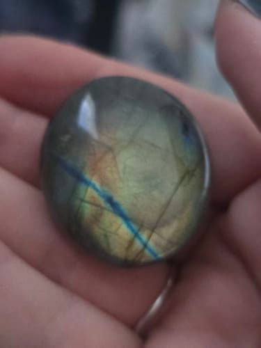 Customer holding a polished, round Labradorite crystal showing a bright blue and yellow iridescent flash.