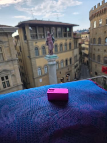 Customer's pink Nano Case resting on a blue cloth with a blurry view of Florence, Italy in the background.