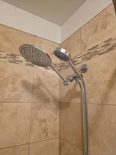 Customer's chrome dual shower head with adjustable arm installed in a tiled shower.
