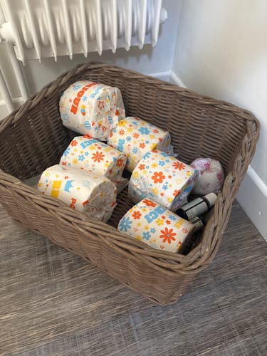 Un client montre plusieurs rouleaux de papier toilette Beau et Doux dans leurs emballages colorés, rangés dans un panier.
