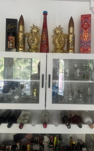 Customer's two gold, bullet-shaped Full Bore Whiskey bottles displayed on a white liquor cabinet.