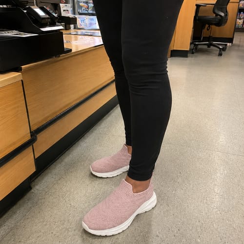 A customer wearing pink Ortho Glide shoes while standing on the hard floor of a retail store.