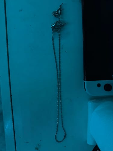 Customer's DANCING WITH DEATH PENDANT necklace lying on a surface under dramatic blue lighting.