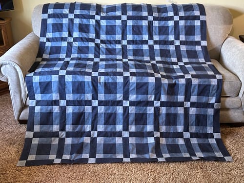 Customer's completed Lockstep quilt in shades of blue and grey, draped over a light-colored sofa.