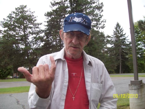 A customer outdoors making a hand gesture while wearing a blue cap and glasses.