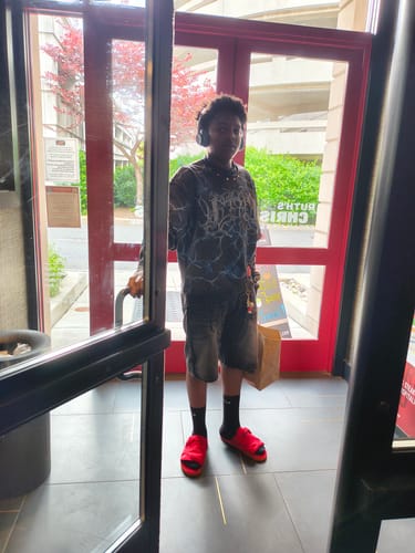 Customer's son wearing comfortable, bright red slides with black socks while standing in a doorway.