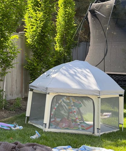 Customer's Pop 'N Go Playpen with sun shade, set up on a grassy lawn with a baby inside.