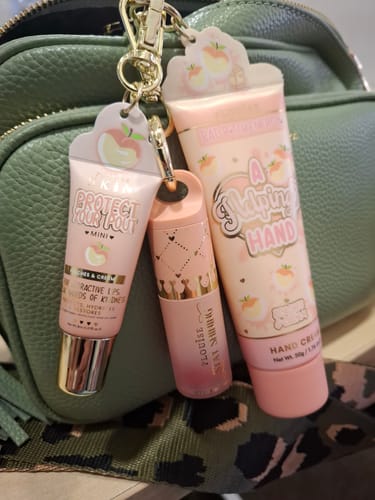 Reviewer shows 'A Helping Hand Cream' and other P.Louise products from the Budget Box clipped onto a green handbag for easy use.