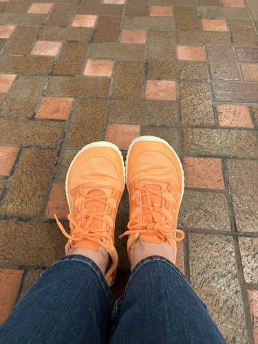 Reviewer's view of their bright orange Forestep Ⅰ Barefoot Shoes, paired with jeans on a tiled floor.
