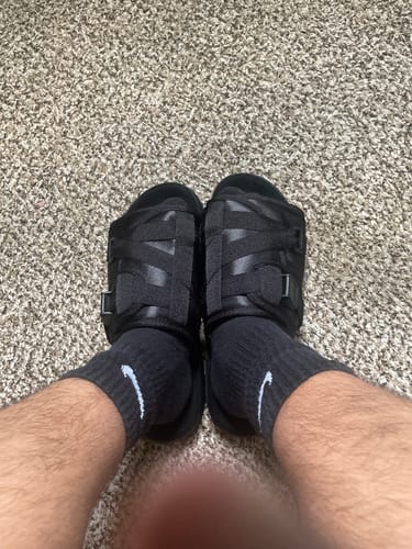Reviewer wearing all-black Blackout Dracos V2 slides with socks on a carpeted floor.