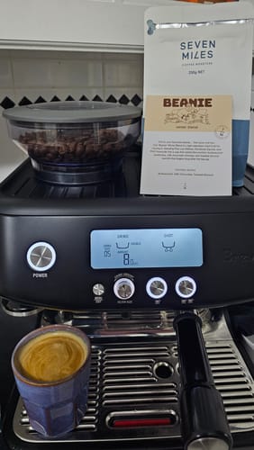 Customer's bag of Winter Blend - Beanie coffee on an espresso machine with a fresh shot brewed in a purple cup.