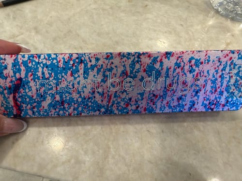 Close-up of a customer's custom Weekly Case with a colorful splatter design and engraved 'might be drugs' text.