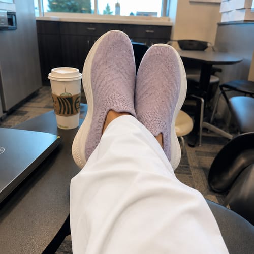 Reviewer relaxing in light purple Ortho Glide™ shoes with their feet up in a clinic breakroom.