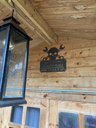 Customer's 'This Is My Happy Place' metal sign hanging on a wooden wall in a summerhouse.