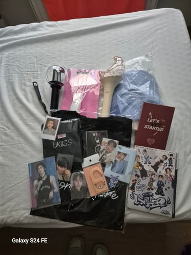 Customer's haul from a K-POP RANDOM BOX, showing lightsticks, photocards, a hat, and other merchandise laid out on a bed.