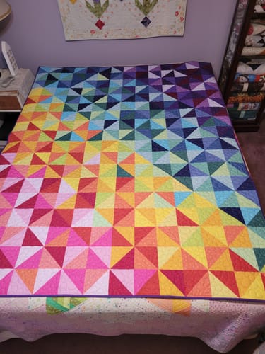 Reviewer's finished Color Study quilt laid on a bed, showing the vibrant geometric pattern in a rainbow gradient.