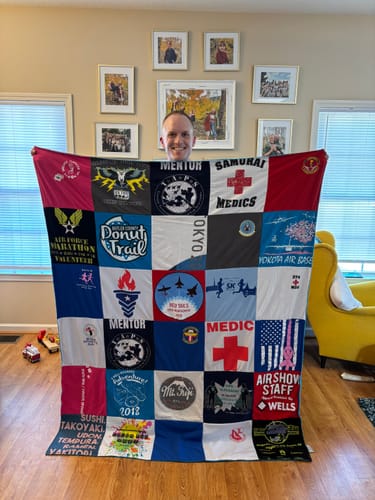 A smiling customer holds up their custom Project Repat T-Shirt Quilt, showing a grid of colorful, memorable t-shirt logos.