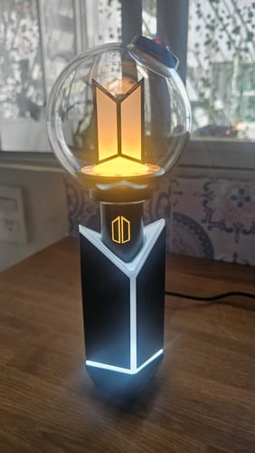 Customer's BTS Official Light Stick Ver.4 illuminated with a warm glow while resting in its lit cradle on a table.