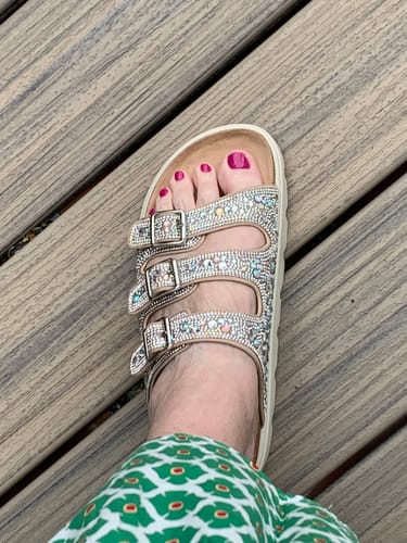 Customer's foot in a sparkly sandal with three buckled straps, seen from above on a wooden surface.
