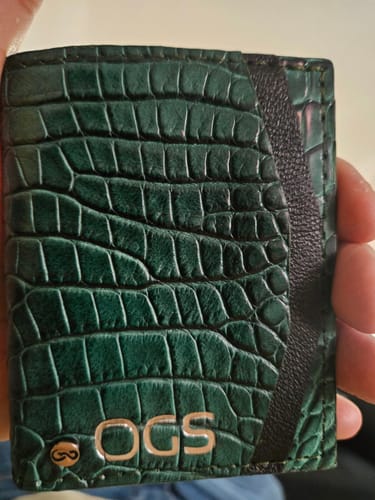 Cliente sosteniendo la Cartera Compacta 'The TIE' de piel verde con textura de cocodrilo.