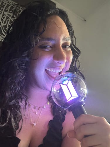 Customer smiling while holding their glowing purple BTS Official Light Stick Ver.4.