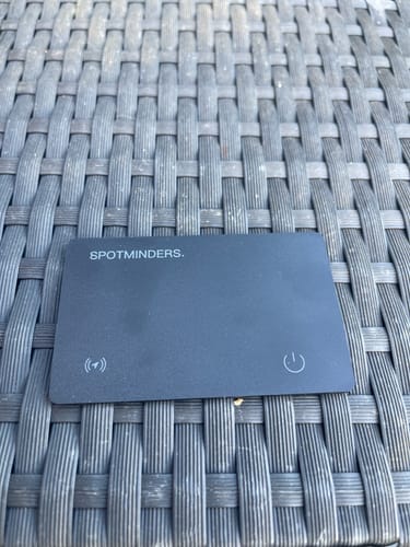 A customer's black SPOTMINDERS Tracking Card resting on a grey woven surface.