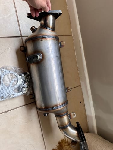 Customer holding the uninstalled DPF delete dummy version over a tiled floor.