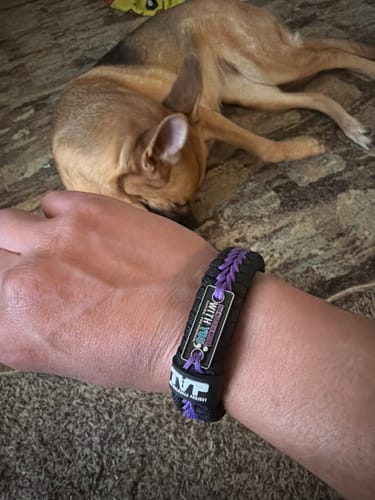 A reviewer's wrist wearing the black and purple Paracord Bracelet, with their small dog resting nearby.