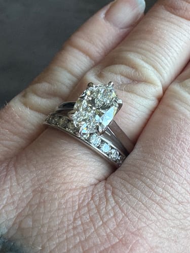 Customer's hand wearing the sparkling DovEggs oval diamond ring with a matching pavé band.