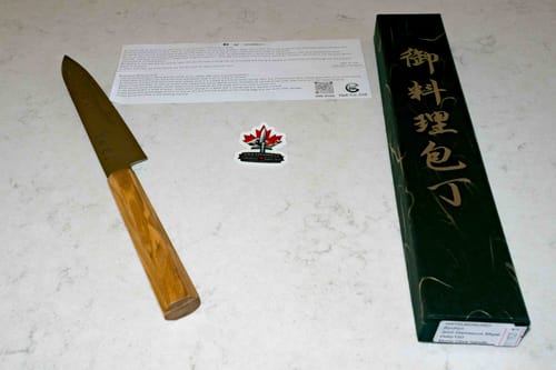 Customer's Ryuhyo Migaki Petty knife with a light wood handle laid on a counter next to its dark green box.