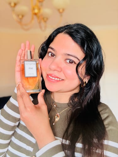 A reviewer smiling while holding a bottle of Inspired by Sauvage Elixir - 926 perfume.
